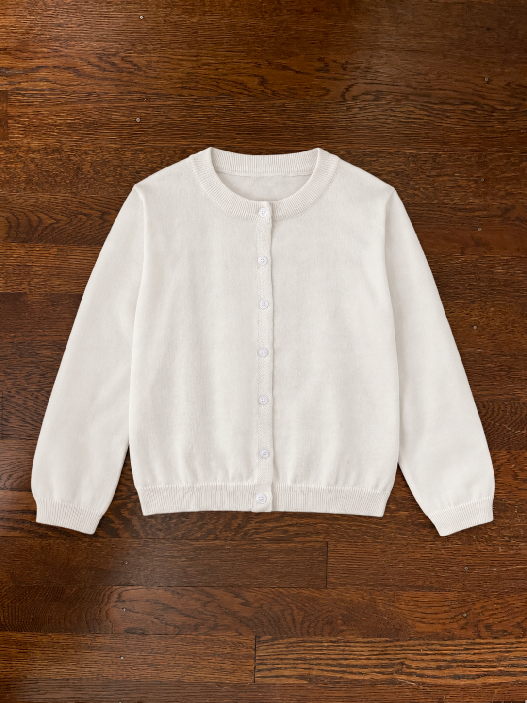 White buttoned cardigan laid flat on a dark wood floor