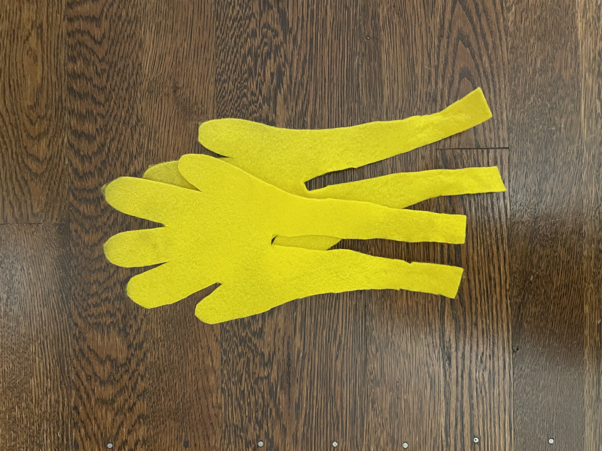 Two cut out yellow felt chicken feet arranged on a dark wood floor